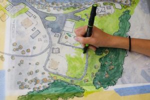 A hand fills in color on a drafted park design