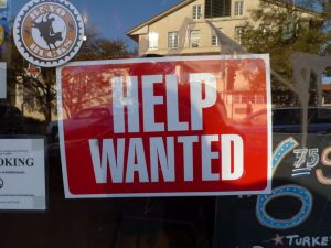 A red sign in a window read "HELP WANTED" in large white text.
