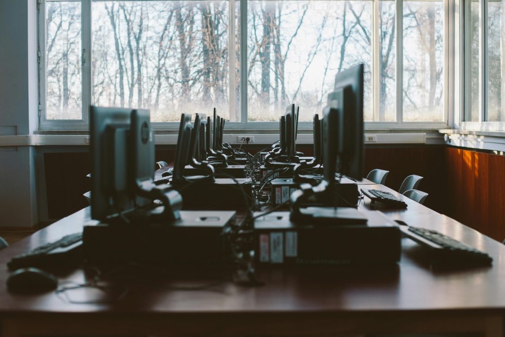 A table of PC desktop computers in front of a window showing a woodsy winter day.