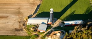 Aerial shot of a farm in Wisconsin. The farm buildings include a red barn, three silos, a shed for animals, a third red building, and a farmhouse.