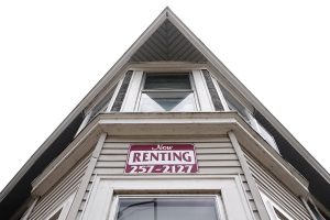 A dramatic upward angle of a House with a Now Renting sign above a window.